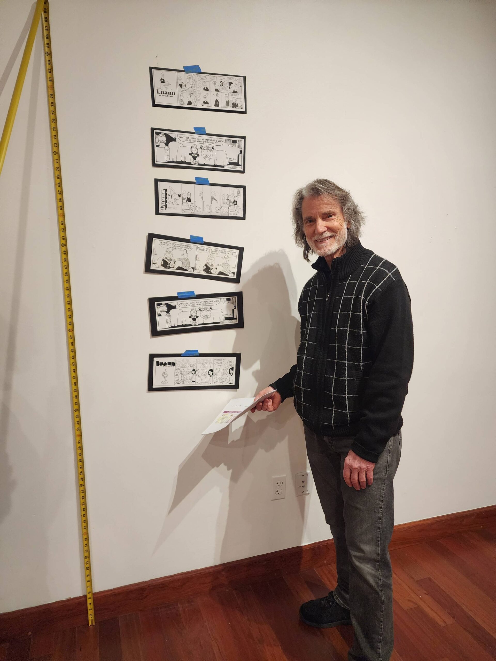Greg stands next to a wall with sample art and a measuring tape.